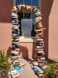 Archway made of books framing a sign that reads "Emerging Writers Festival 2019, Old Town Alexandria, VA"