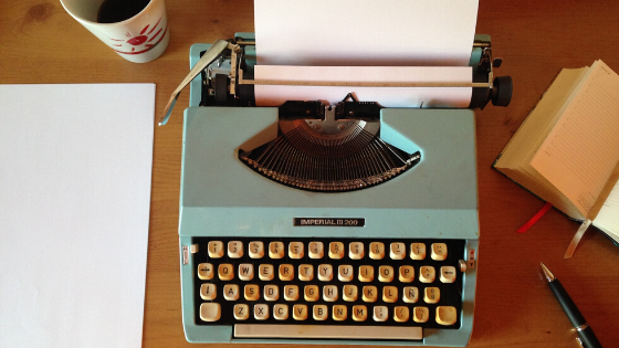 Cover image of a coffee cup, a teal typewriter, and a journal with a pen all lying on a table