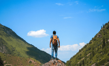 Man in hiking clothes standing on top of a rock, looking out over mountains